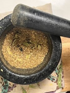 Coarsely ground roasted spices with cardamom, cumin, and coriander in a black mortar and pestle.