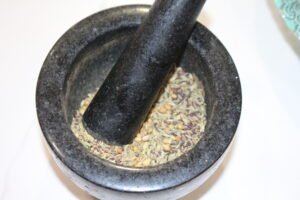 Whole coriander, cumin, mustard, and fenugreek seeds in a mortar with pestle.