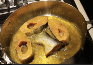 Fish pieces frying in hot oil in a cooking pot.